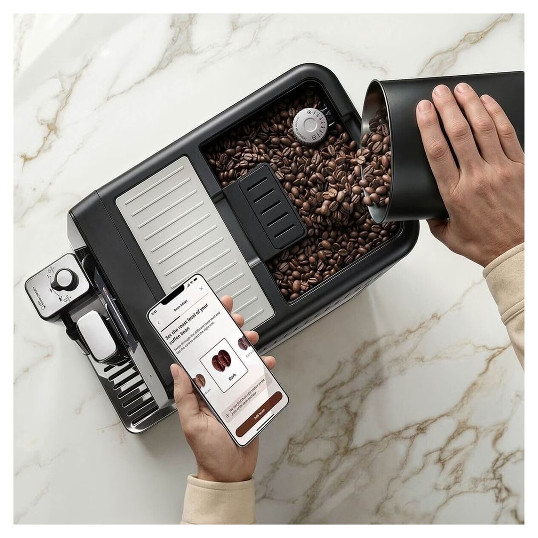 Hands pouring coffee beans into a coffee machine while holding a smartphone