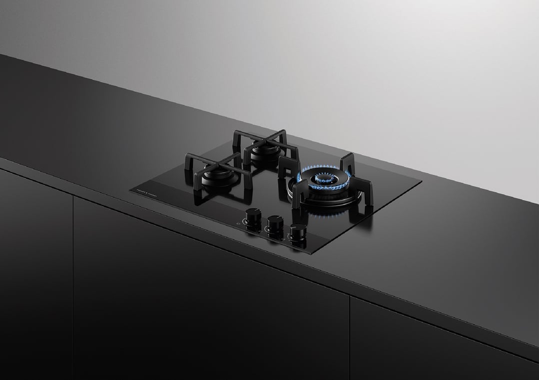 Black gas on glass cooktop with three burners, one lit, in a modern kitchen