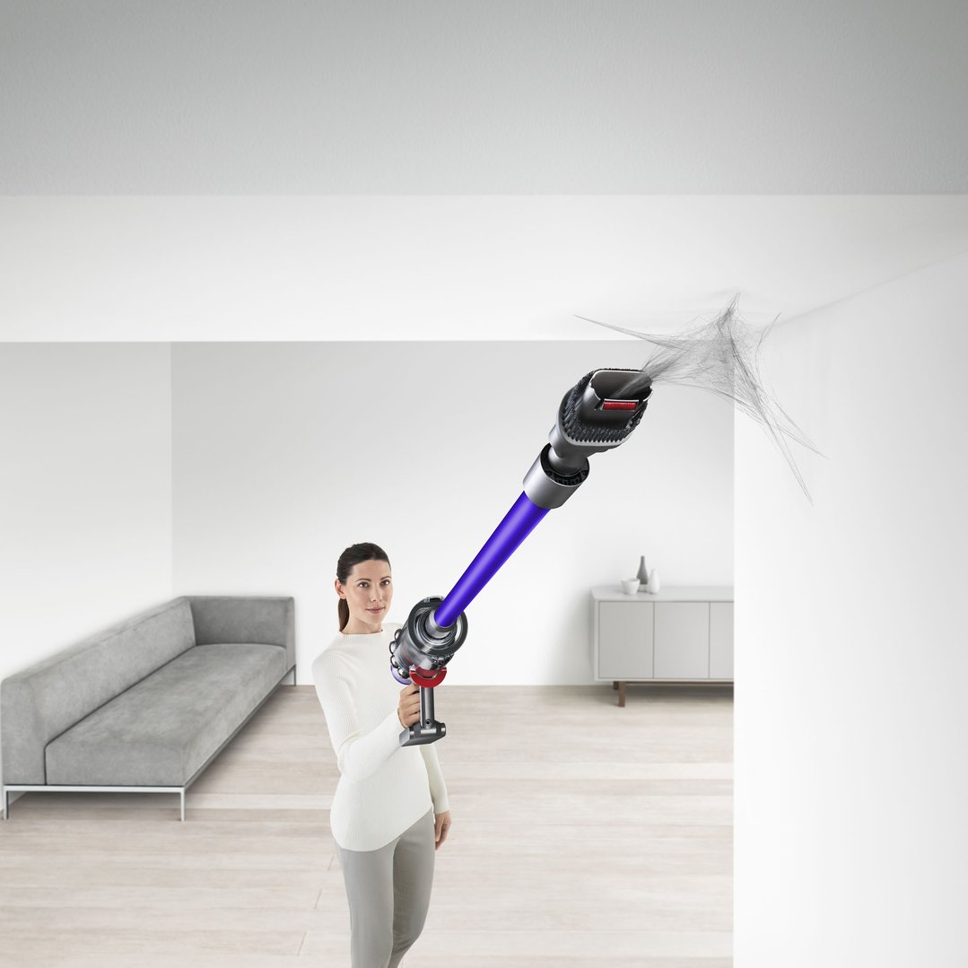 Woman using a Dyson V11 stick vacuum to clean cobwebs from a ceiling