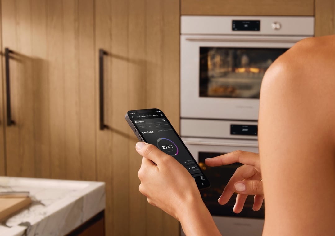 Person holding a smartphone displaying a cooking app in front of an oven