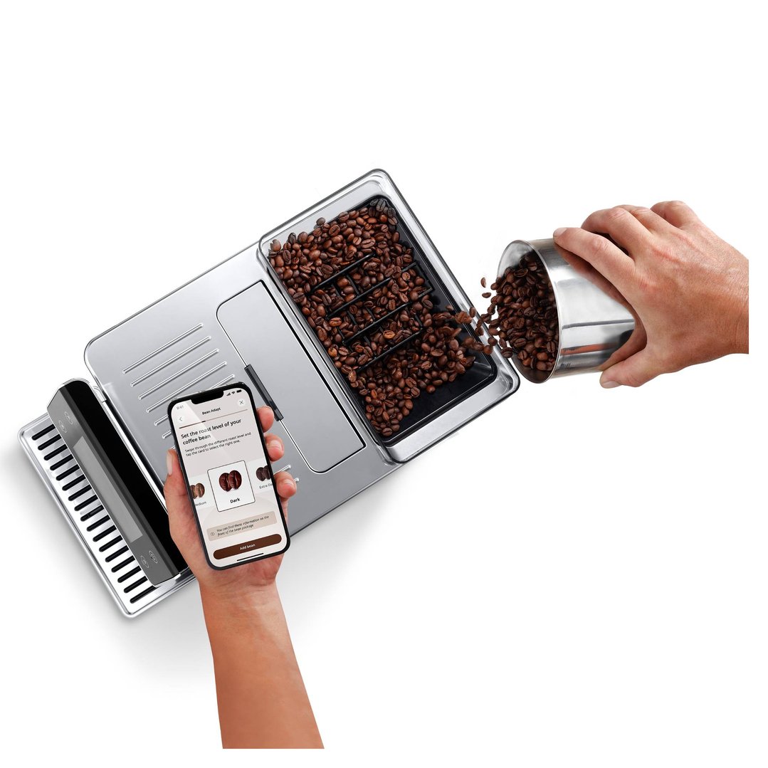 Hands pouring coffee beans into a coffee machine, with a phone displaying an app