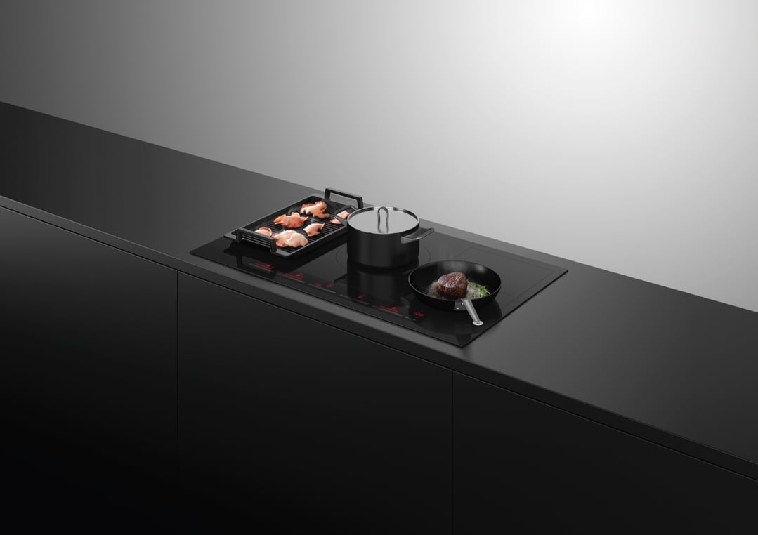 Induction cooktop with a grill pan, pot, and frying pan in a dark kitchen