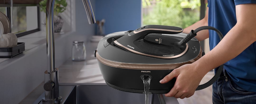Person emptying water from a Philips PerfectCare Steam Generator 8000 Series iron into a sink