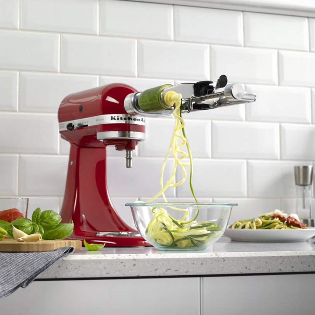 Red KitchenAid stand mixer with spiralizer attachment making zucchini noodles in a kitchen