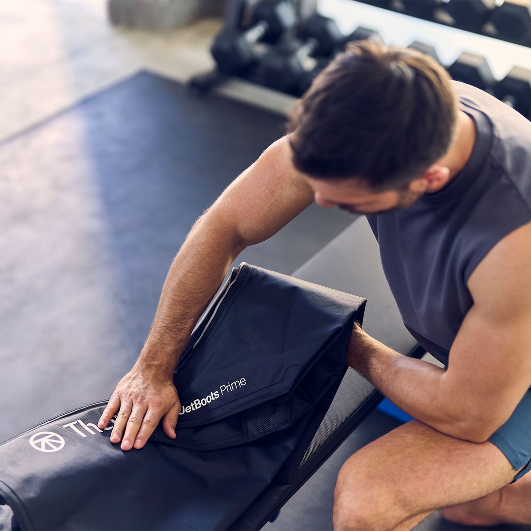 Man opening a black JetBoots Prime massager case in a gym