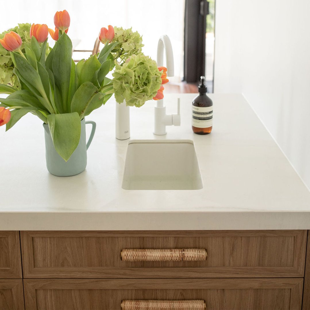 White fireclay sink in a kitchen island with flowers and soap dispenser