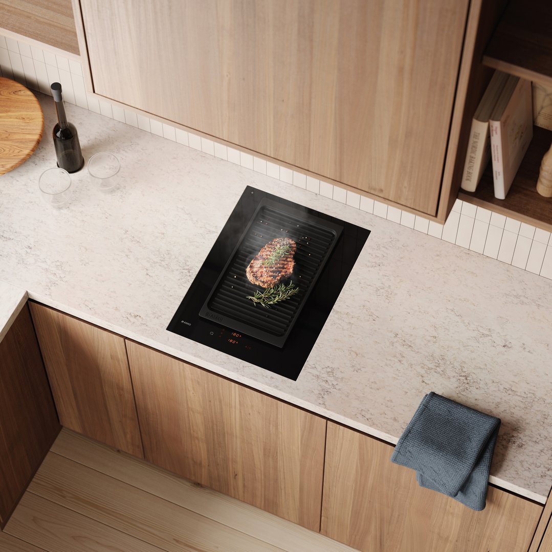 An ASKO induction cooktop with a steak grilling on a griddle in a modern kitchen