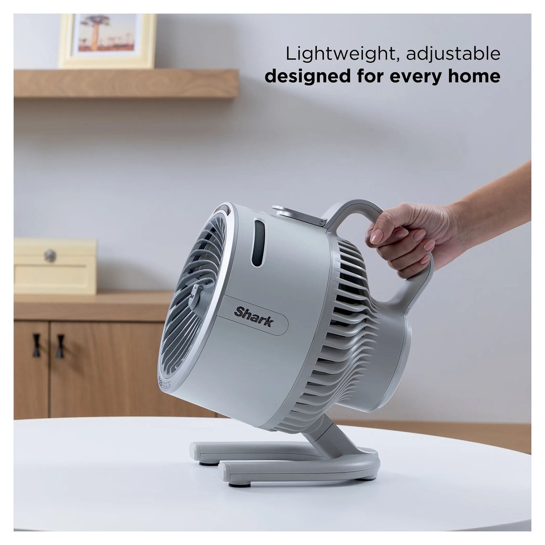 Hand holding a Shark portable fan on a white table indoors