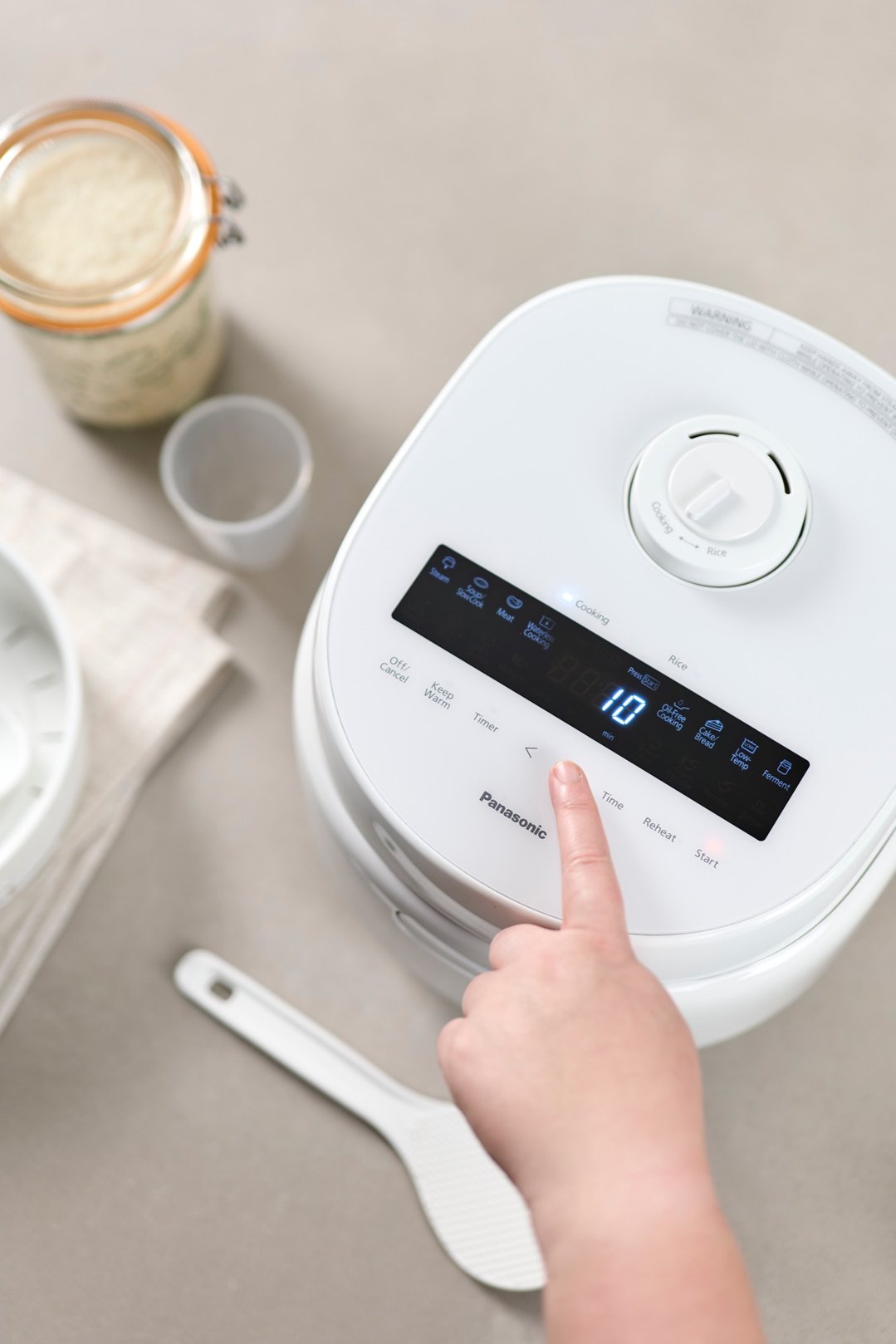 A hand pressing a button on a white Panasonic rice and multi cooker