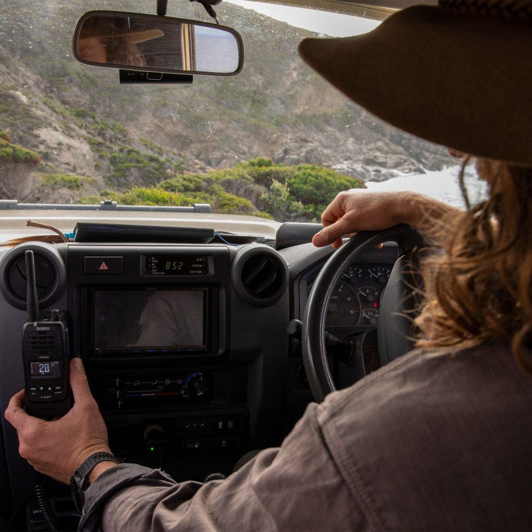 Person holding a Uniden two-way radio inside a vehicle with a scenic view