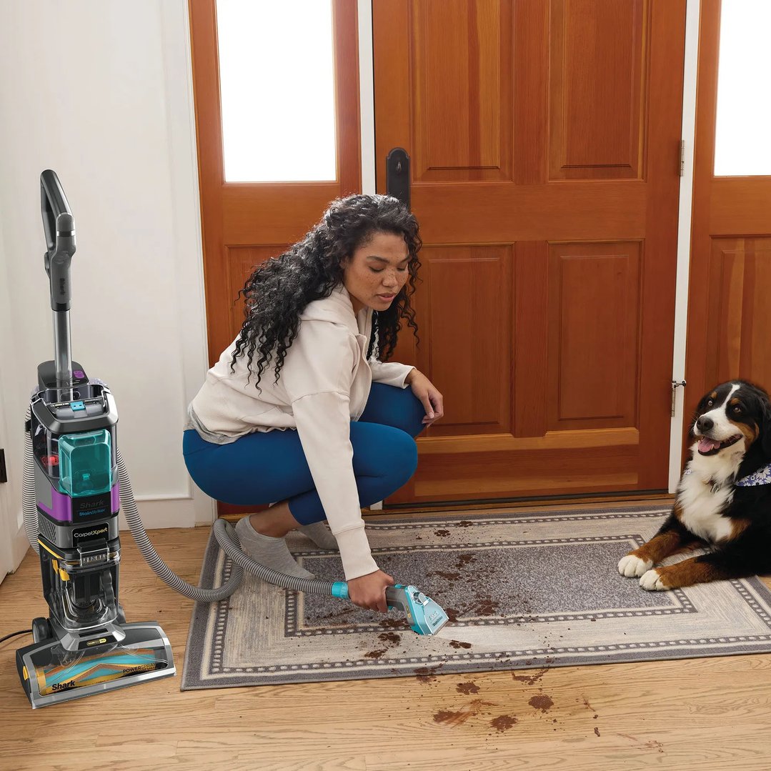 Woman cleaning a dirty rug with a Shark CarpetXpert vacuum cleaner, dog nearby