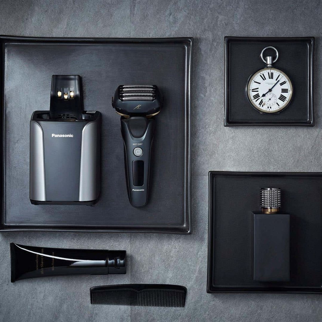 Panasonic shaver and charging station with grooming accessories on a grey surface