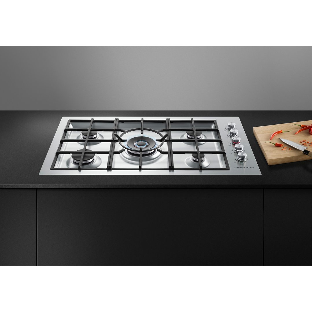 Stainless steel 5 burner gas cooktop with one burner lit, on a black countertop