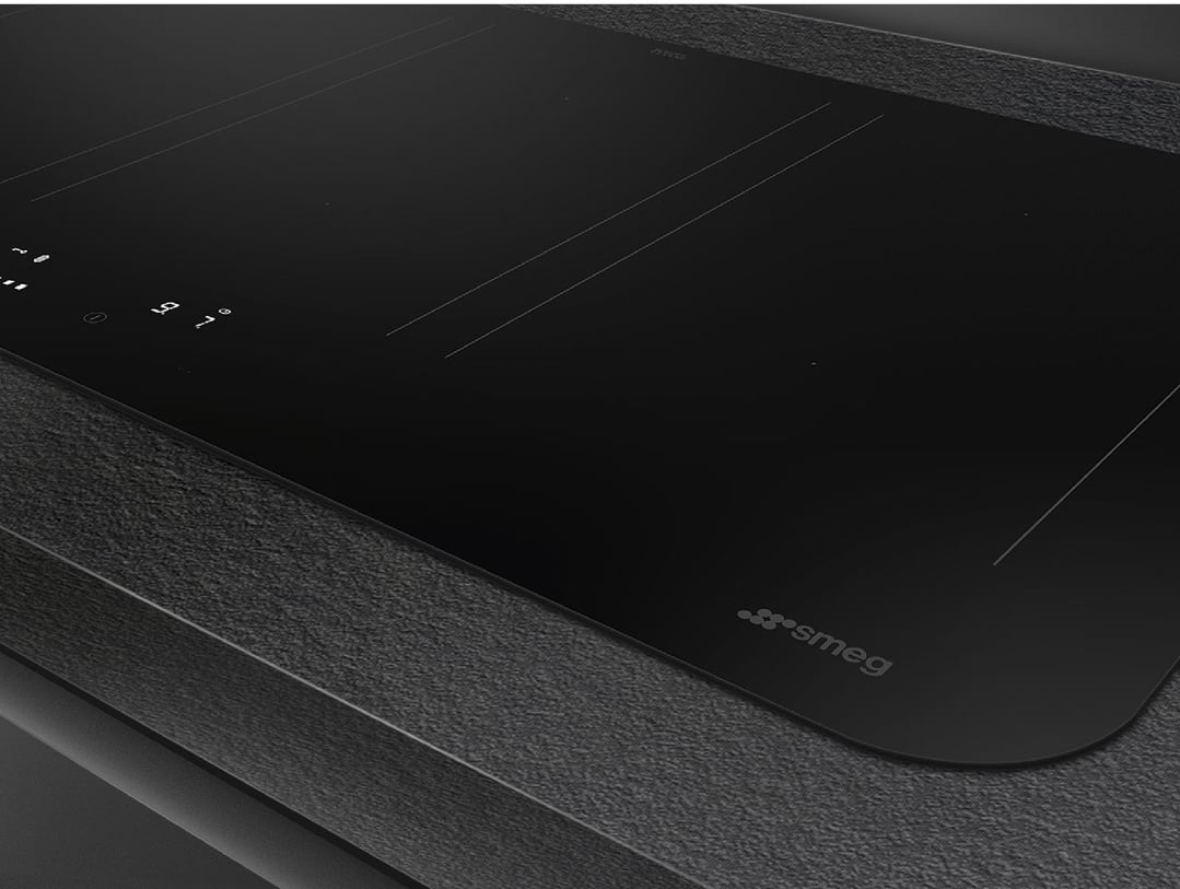 Close up of a black induction cooktop with controls on a dark countertop