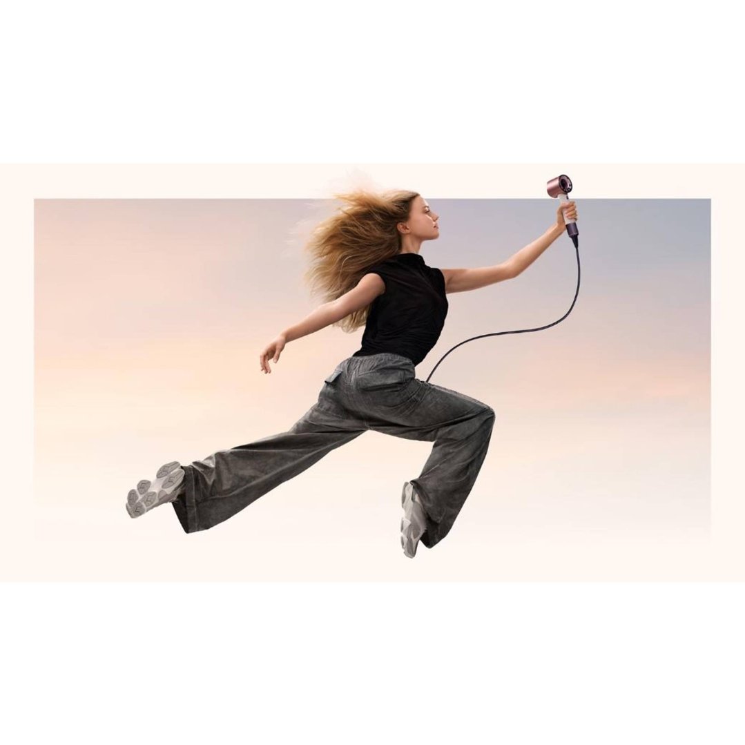 Woman in black top and grey pants jumping, holding a hair dryer