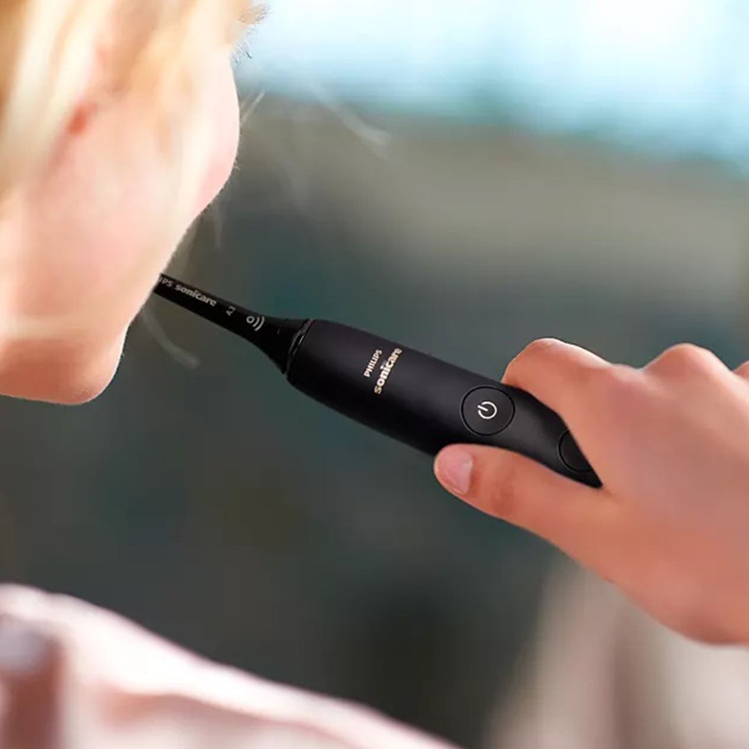 A person holding a black Philips Sonicare electric toothbrush to their mouth