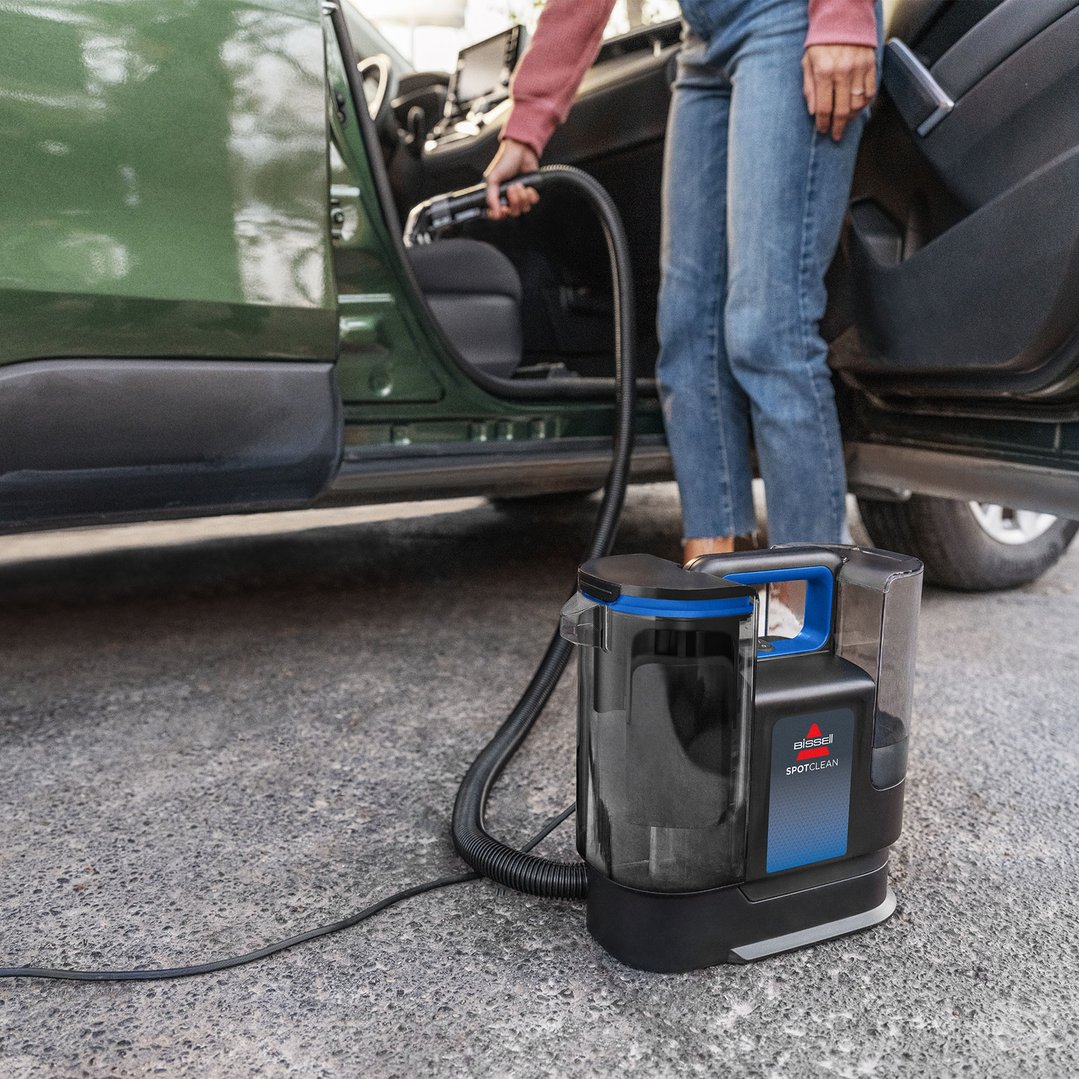 Person cleaning the interior of a green car with a BISSELL SpotClean vacuum cleaner