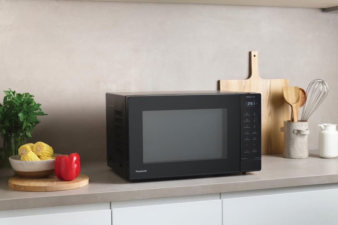 Black Panasonic microwave on a kitchen counter with vegetables and utensils