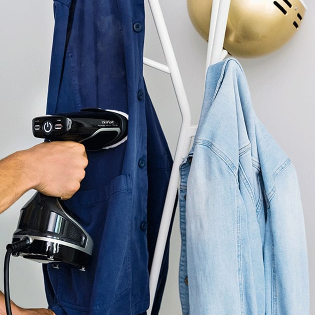 Hand holding a Tefal garment steamer to a blue shirt