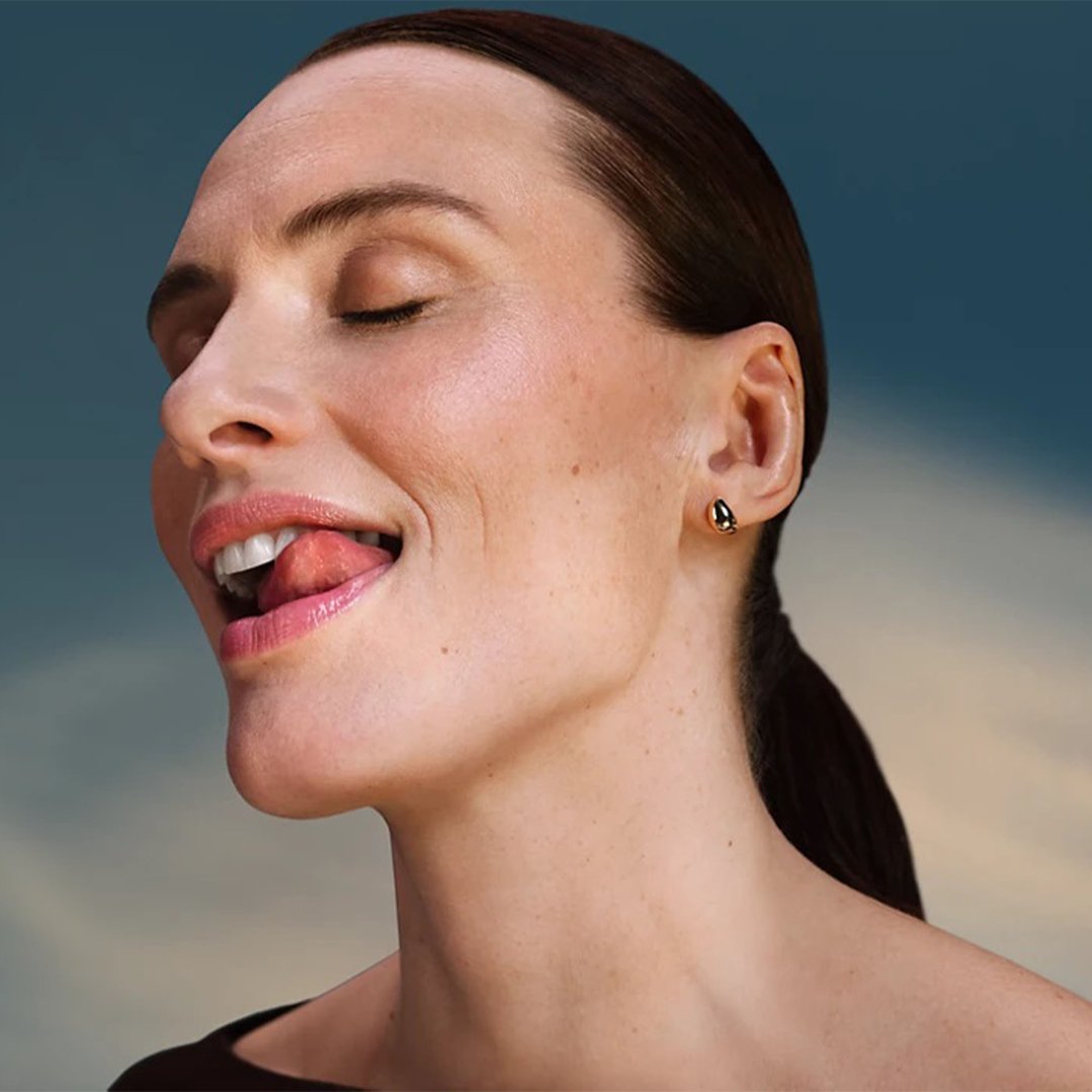 Woman with closed eyes and tongue out, wearing a gold earring
