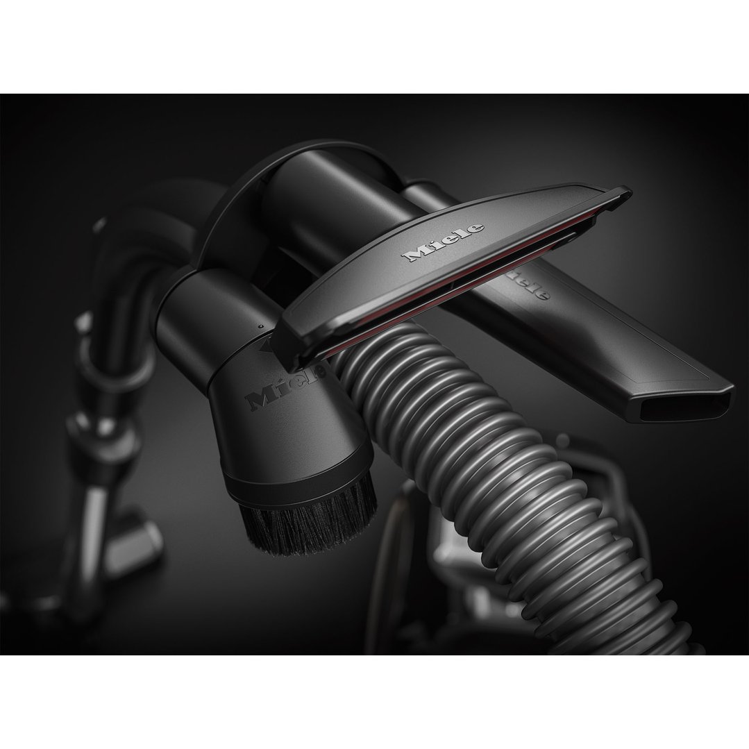 Close-up of the Miele vacuum cleaner's hose and attachments on a dark surface