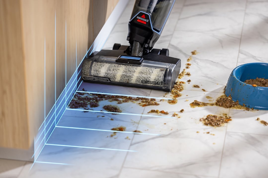BISSELL handStickVacuum cleaning up spilled pet food on a tiled floor next to a wall
