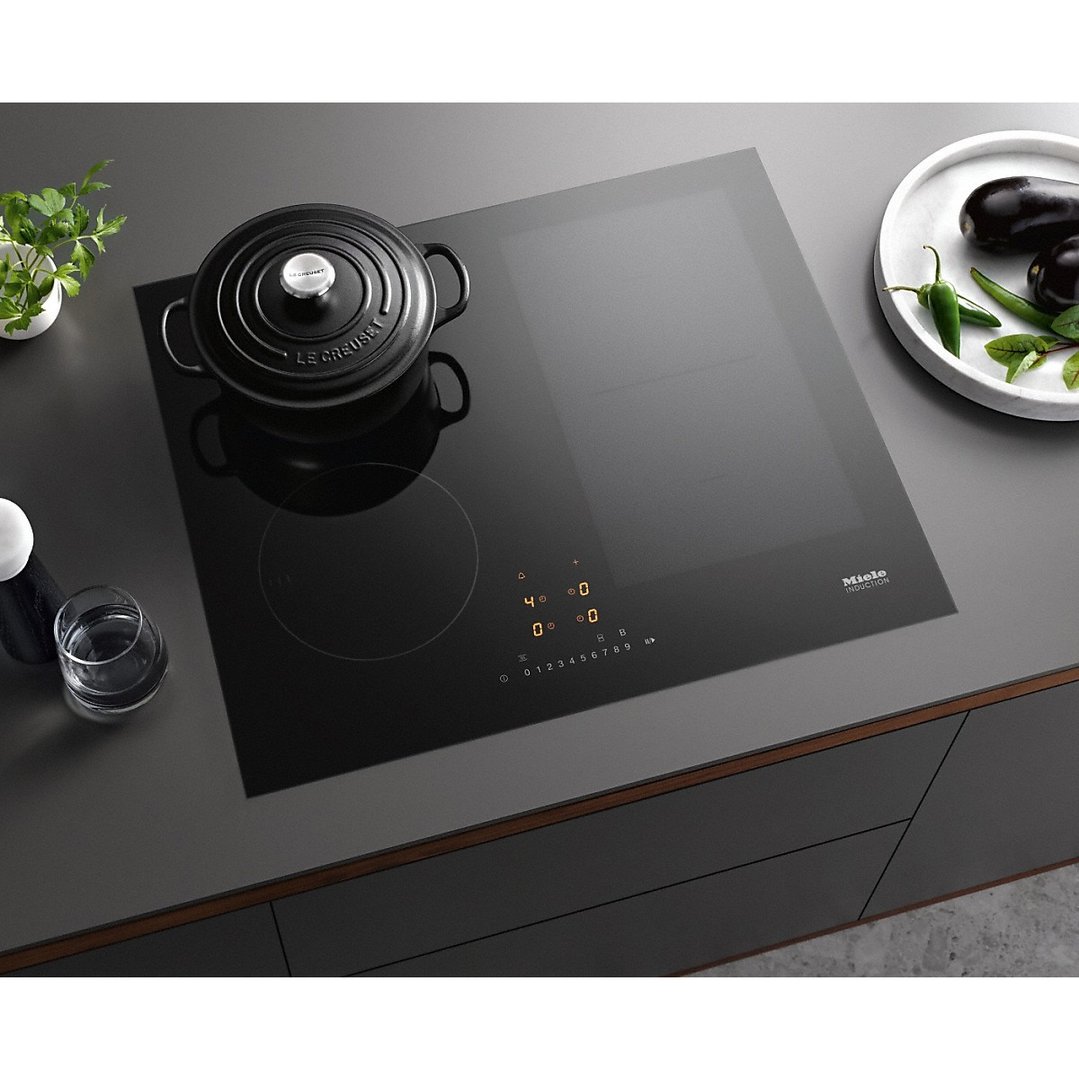 Black induction cooktop with a pot and vegetables on a dark countertop