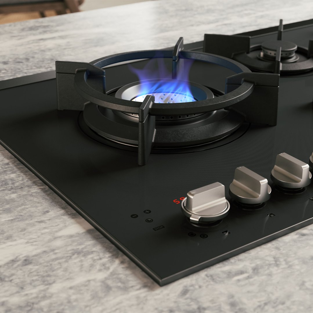 Gas cooktop with blue flames on a burner, integrated into a marble countertop