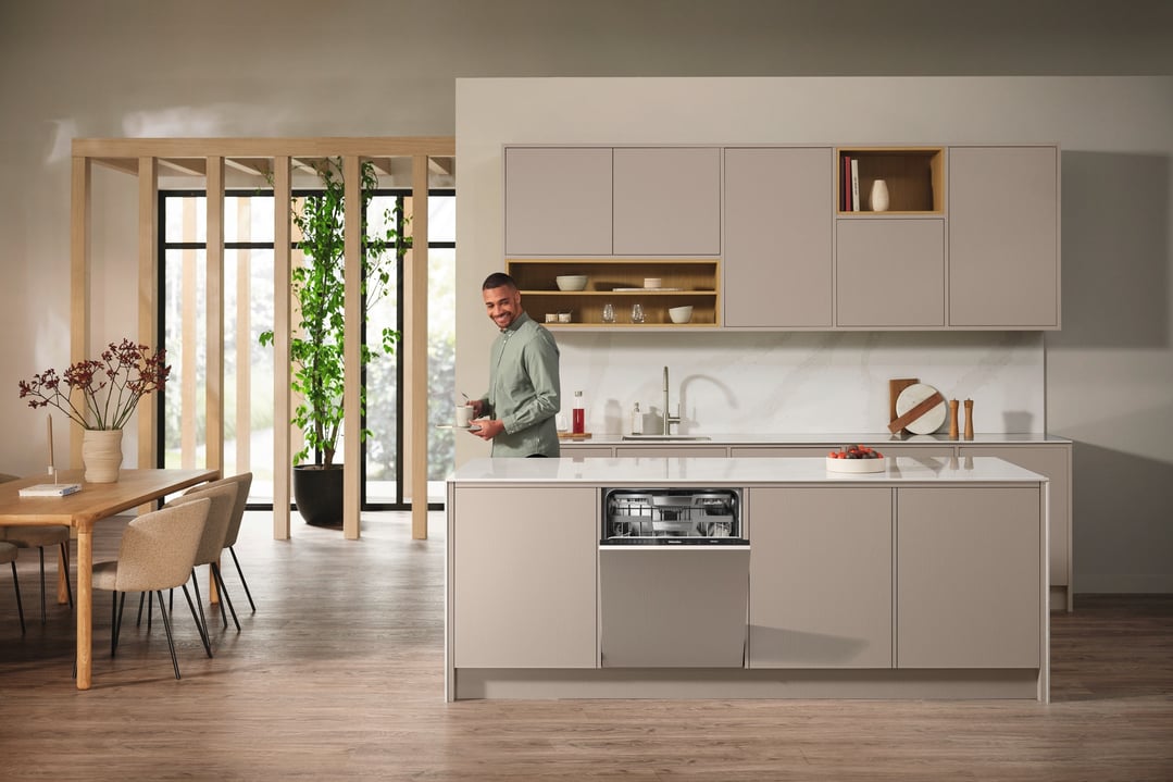 Man holding a cup and plate in a modern kitchen with a built-in dishwasher