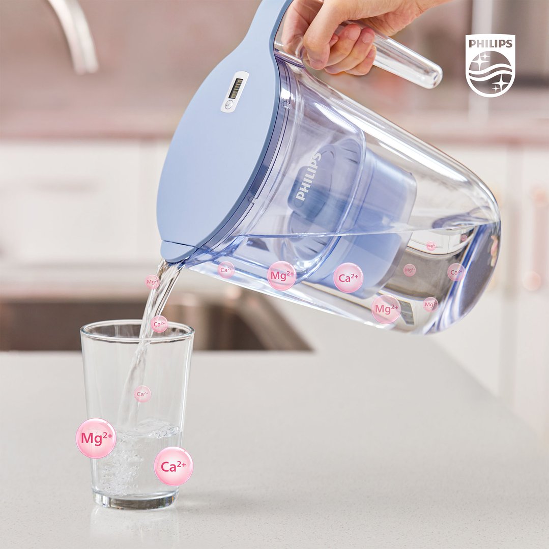 Hand pouring water from a Philips water filter pitcher into a glass