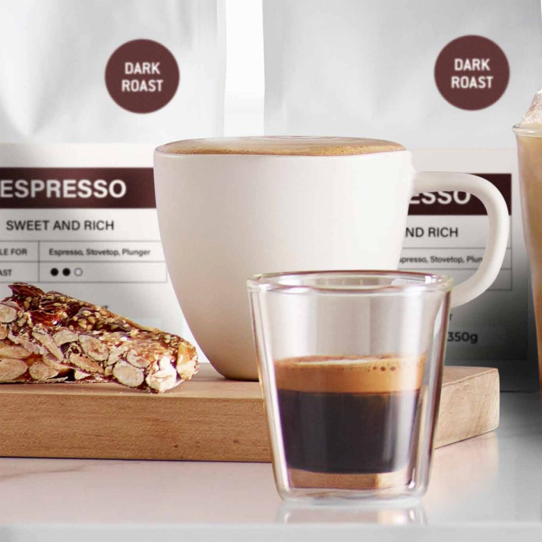 Espresso in a dual wall glass and a mug with coffee bags and a snack