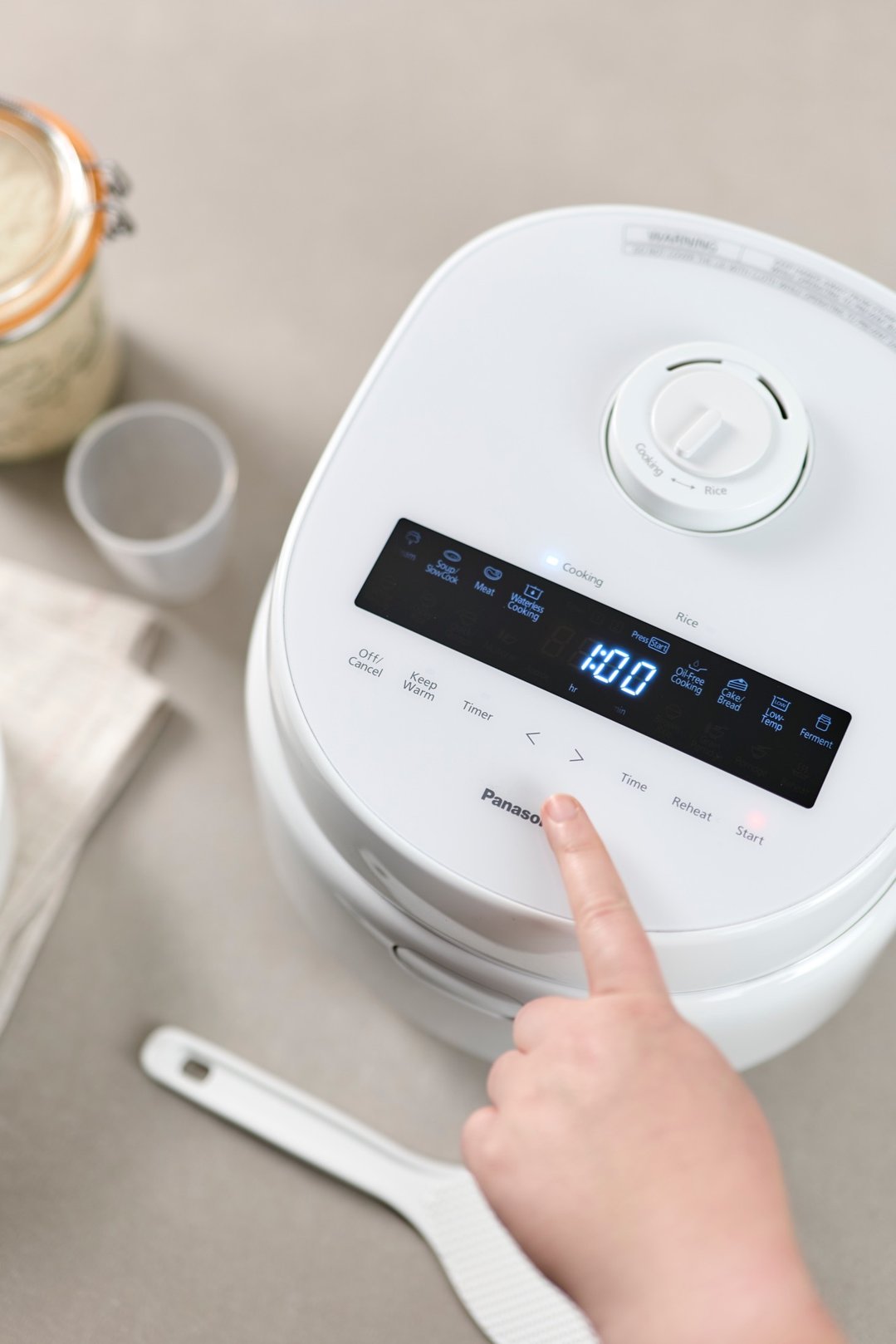 Hand pressing button on a white Panasonic rice and multi cooker