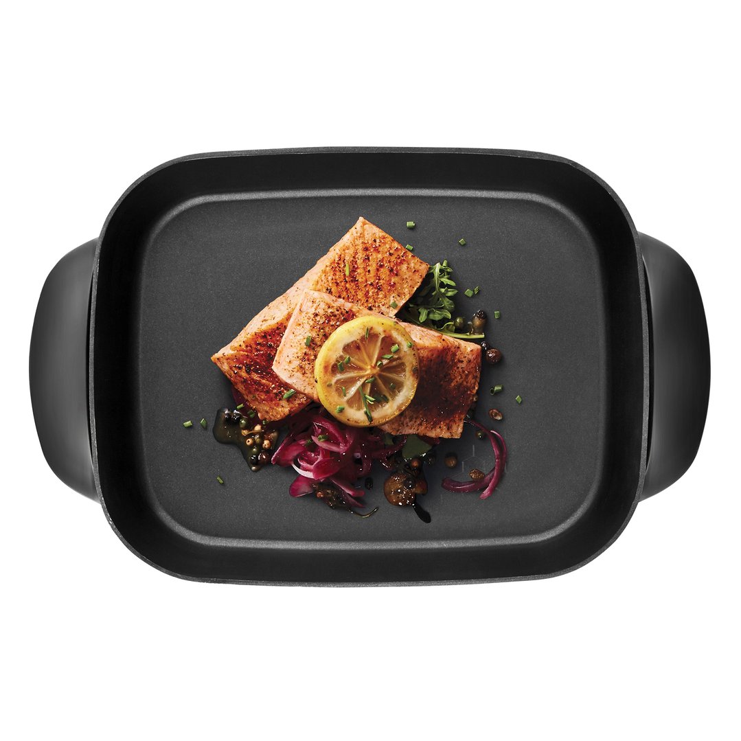 Overhead view of a black electric frypan with cooked salmon and garnishes