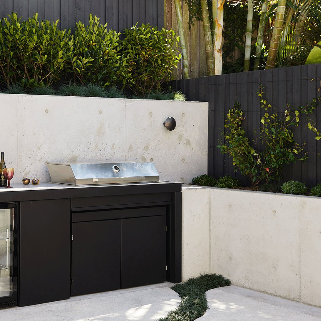 Built-in BBQ on an outdoor kitchen counter with concrete walls and plants