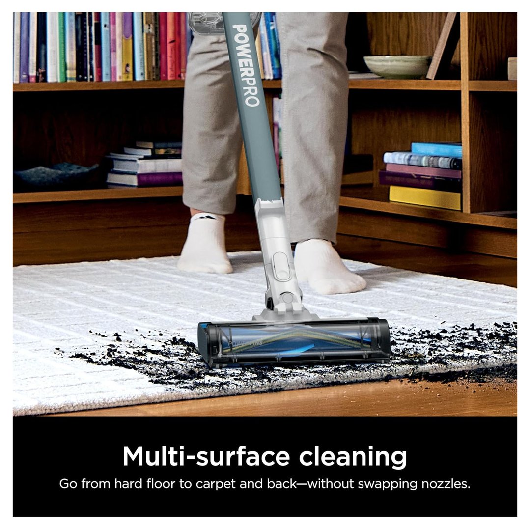 Person using a Shark PowerPro cordless stick vacuum to clean a dirty white rug