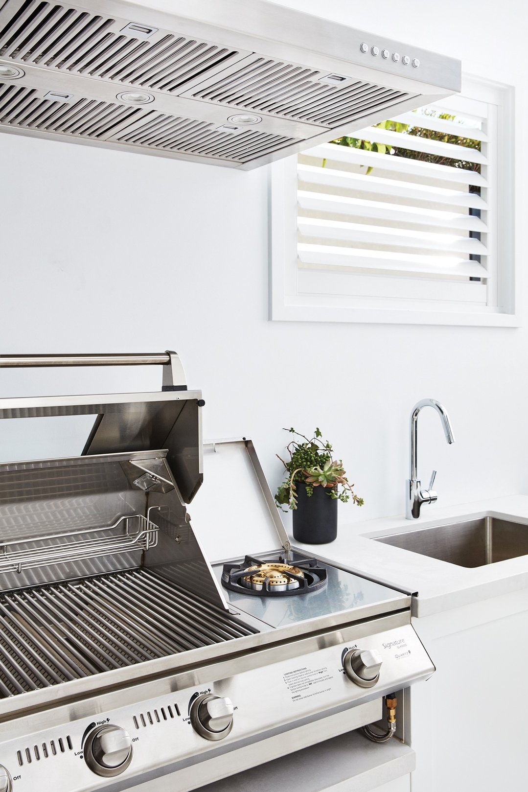 Stainless steel rangehood mounted above an outdoor grill and sink area