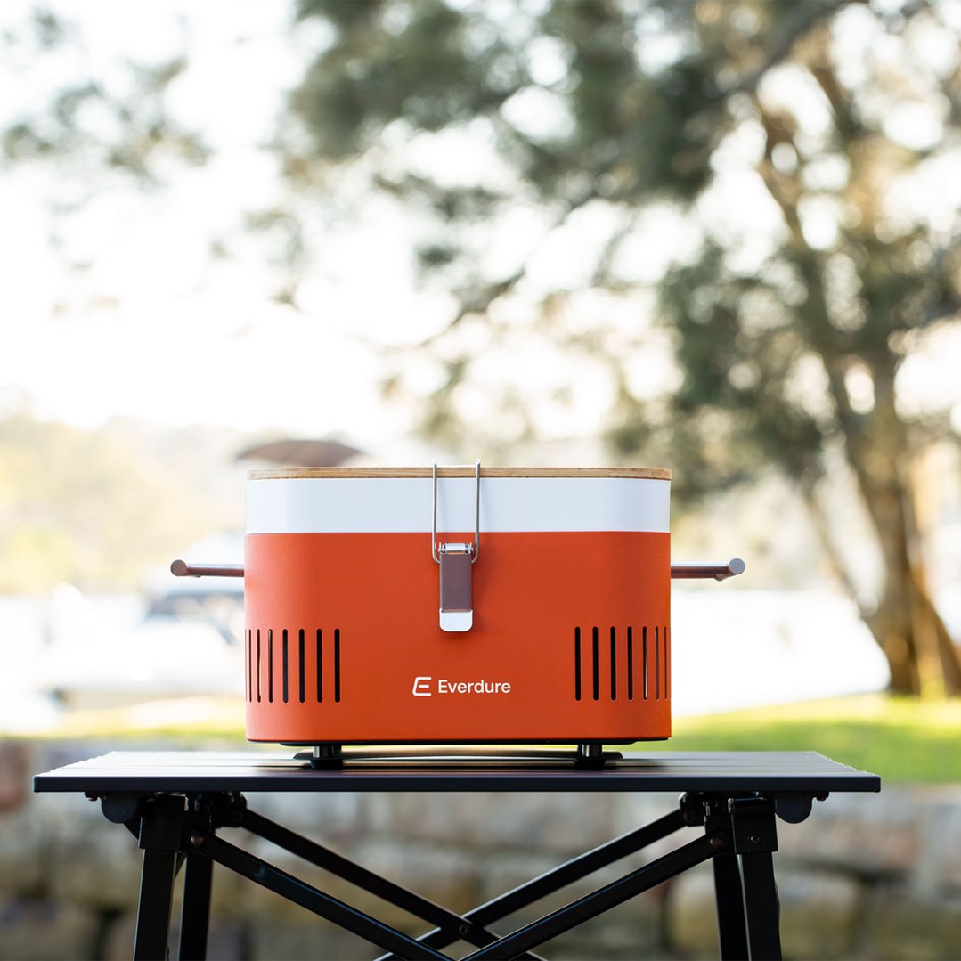Orange Portable Charcoal BBQ on a black table outdoors with blurred background