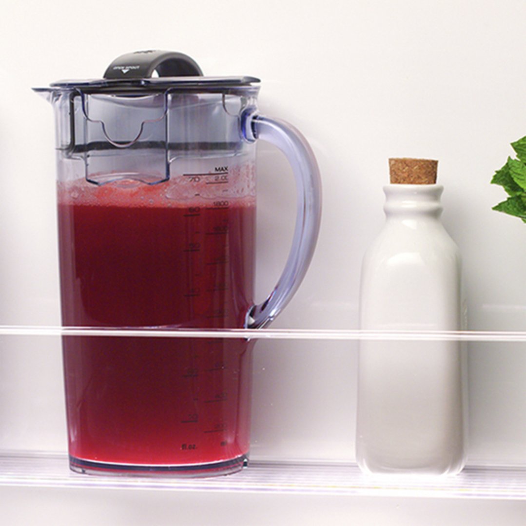Juicer filled with red juice next to a white bottle in a refrigerator