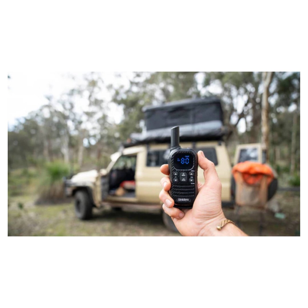 Hand holding a Uniden UHF radio with a vehicle and trees in the background