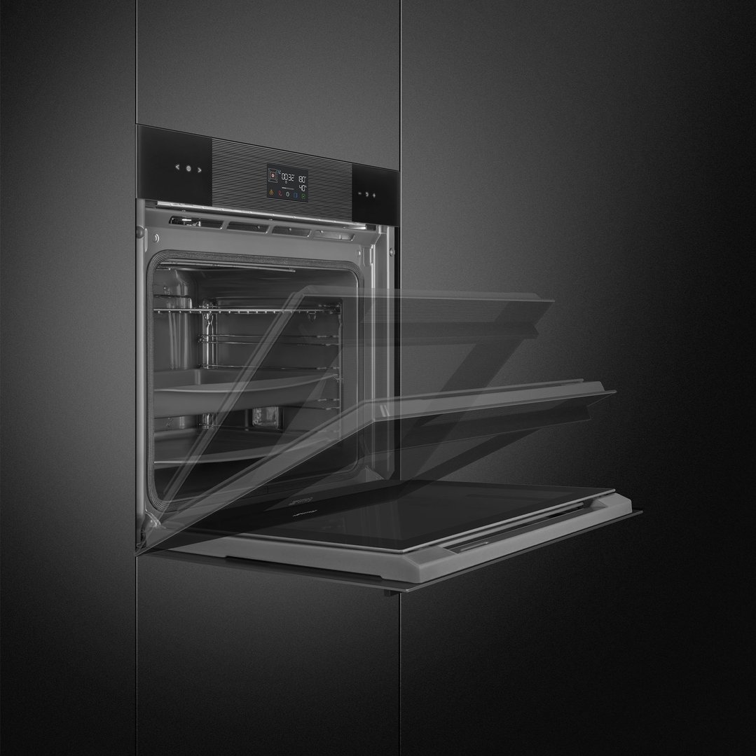 Black built-in oven with door partially open in a dark kitchen