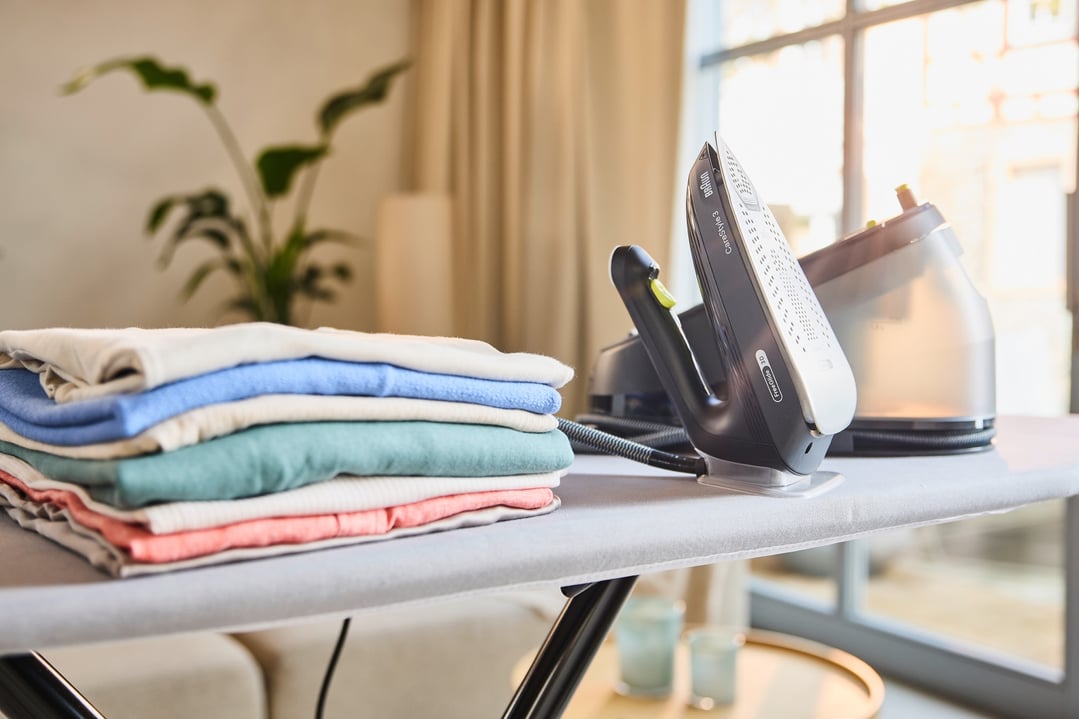 Braun CareStyle 3 steam generator iron on an ironing board with folded laundry