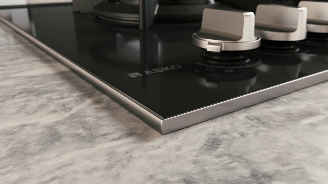 Close up of a black glass cooktop with silver controls on a marble countertop