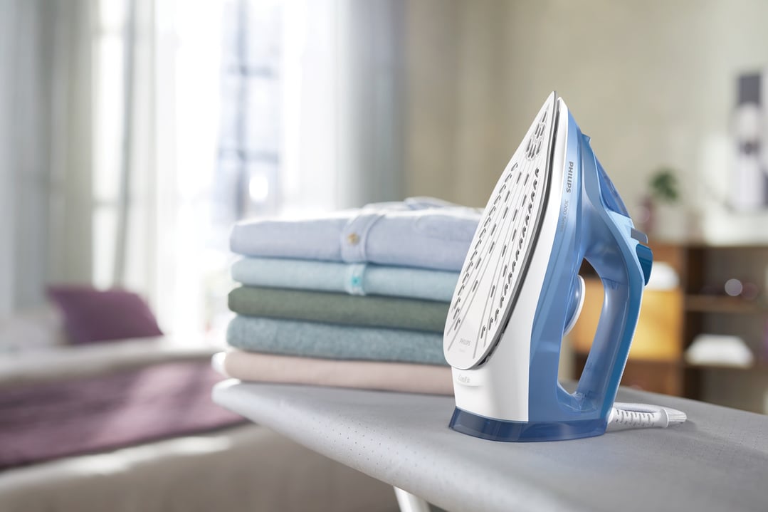 Blue Philips 3000 Series steam iron on an ironing board with folded clothes
