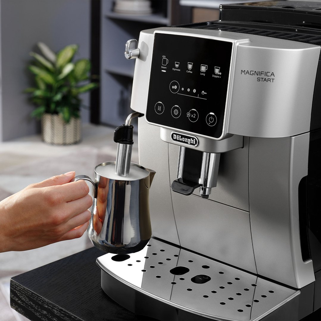 Hand holding a milk frothing jug under the steam wand of a coffee machine