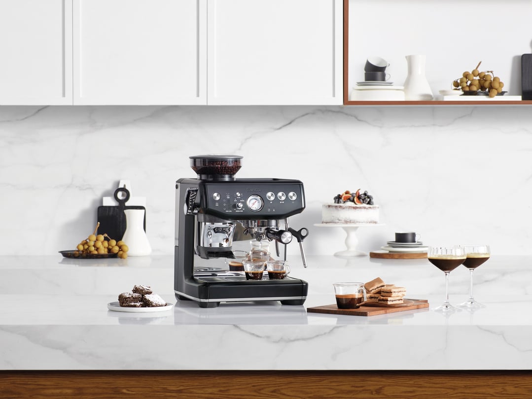 Breville Barista Express Impress coffee machine on a kitchen counter with desserts
