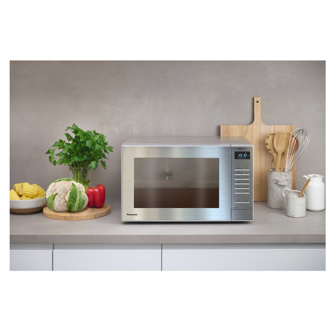 Stainless steel microwave on a kitchen counter with vegetables and kitchen utensils