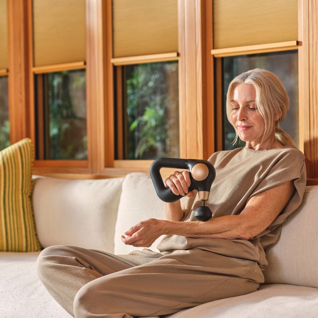 Woman sitting on a couch using a massager on her arm