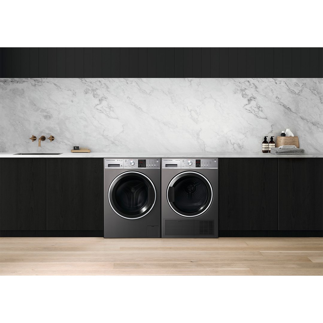 Two dryers in a modern laundry room with marble backsplash and dark cabinetry