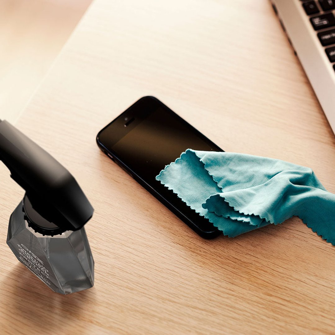 Black spray bottle and blue cloth cleaning a smartphone on a wooden surface