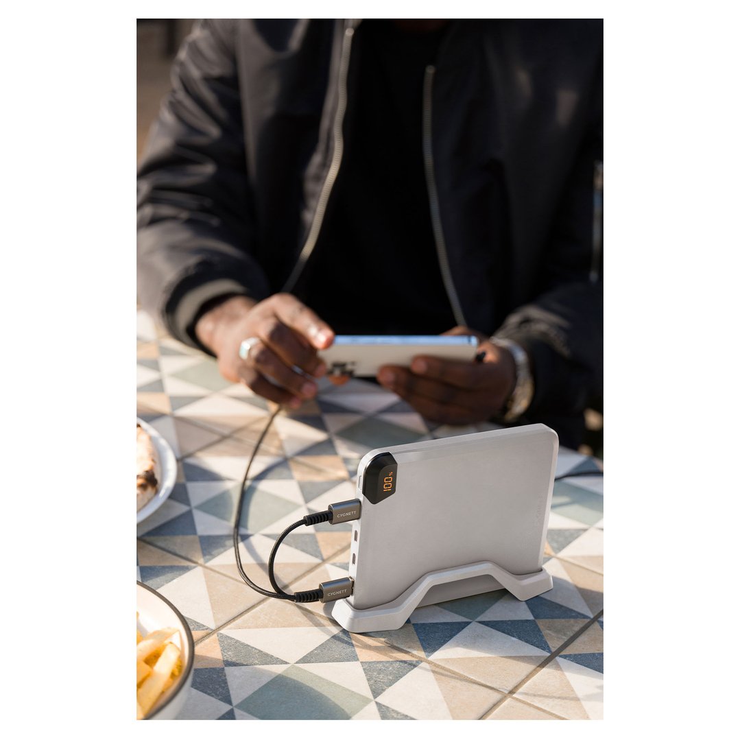 Man charging phone with a power bank on a patterned outdoor table